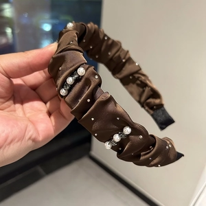 Close-up of brown satin headband with pleats, sparkling rhinestones and white pearls