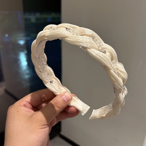 Close-up of cream braided headband with satin texture and elegant clear bead accents