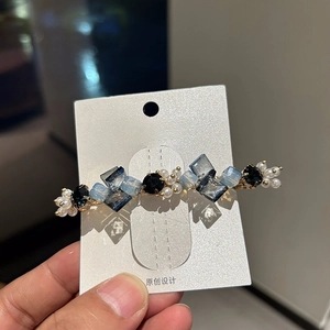 Detail view of handmade long hair clip with blue crystals and pearls on gold base