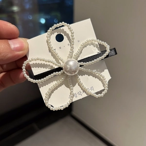 Détail d'une pince à cheveux noire élégante ornée d'une fleur de perles blanches