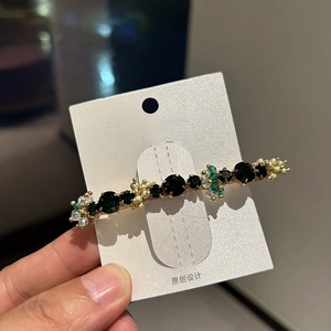 Close-up of golden hair clip with dark green gemstones and sparkling clear crystals