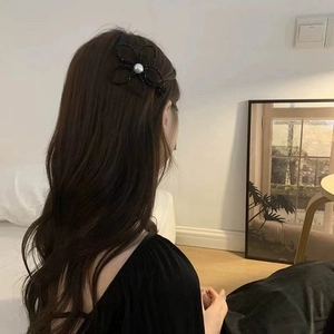 Détail d'une pince à cheveux fleur en perles noires avec perle blanche sur une femme