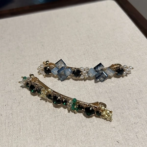 Detail view of handmade hair clips featuring blue and green crystals with pearl accents
