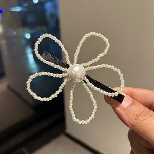 Détail d'une pince à cheveux fleur en perles avec ruban noir sur une base en métal