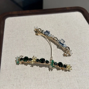 Close-up of luxury crystal hair clips with emerald stones and pearls on metal base