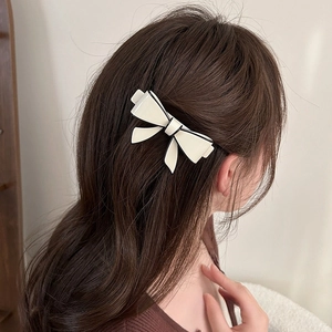 Close-up of a cream acetate bow hair clip with black edges worn on a model's hair