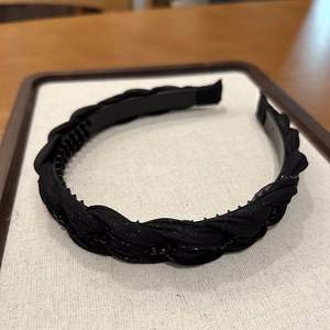 Detail of black braided headband with satin texture and anti-slip plastic teeth