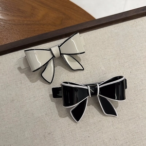 Close-up of acetate bow hair clips in cream and black showing glossy resin texture