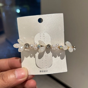Detailed shot of gold hair clip with crystal leaves and faux pearls on white card