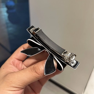 Close-up of black acetate bow hair clip with white piping and silver metal spring clip