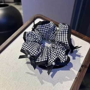 Detail of checkered scrunchie with black ribbons and white pearls on a tray
