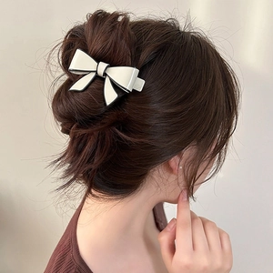 Elegant cream bow hair clip with black edges shown in a sophisticated hair style