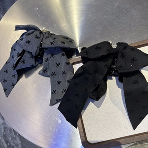 Detail view of large bow hair claws in black and grey fabric with pearl and metal logo charm
