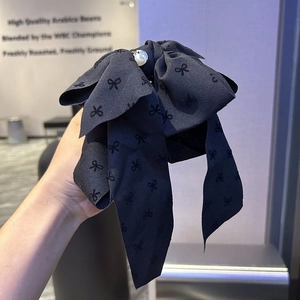 Detail of black satin bow hair clip featuring jacquard pattern and white pearl center