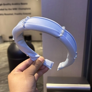 Detail of light blue padded headband featuring decorative pearls and silky fabric texture