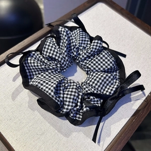 Detailed view of gingham checkered scrunchie with elegant black satin bow hair accessory