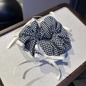 Detail of black and white gingham scrunchie featuring cream ribbon bows on a display tray