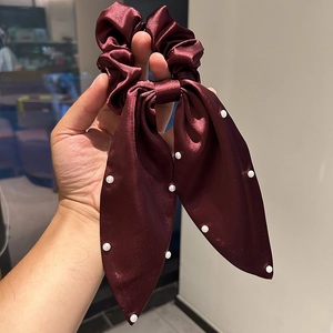 Détails de la texture satinée et des perles blanches sur le chouchou en soie bordeaux