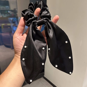 Détail d'un chouchou en satin noir avec accents de perles blanches et texture soyeuse