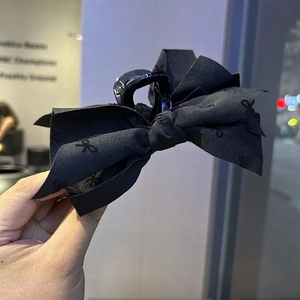 Detail of oversized black bow hair claw clip with satin pattern and glossy grip