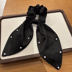 Détail d'un chouchou en satin noir avec rubans longs et perles blanches décoratives