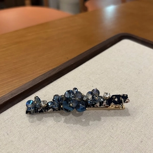Detailed close-up of handmade hair clip with deep blue crystals on vintage fabric base