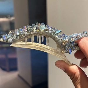 Close-up of luxury crystal hair claw clip with colorful resin teeth and floral fabric details