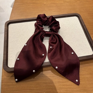 Détail d'un chouchou en satin bordeaux orné d'élégantes perles blanches sur le ruban