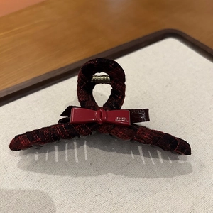 Detailed close-up of a red and black plaid tweed hair claw with a small resin bow accent