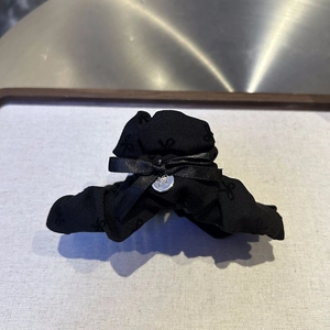 Close-up of black fabric hair claw clip with satin bow and silver metal logo charm