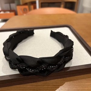 Détail d'un serre-tête tressé noir avec des perles scintillantes sur un support clair