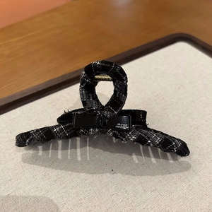 Detailed close-up of houndstooth fabric hair claw clip with black bow and gold text