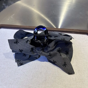 Detail of grey bow hair claw clip with black butterfly prints on a beige textured mat