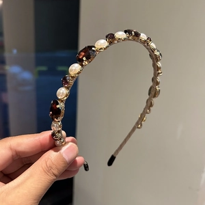 Elegant gold headband with pearls and brown rhinestones held in hand for women