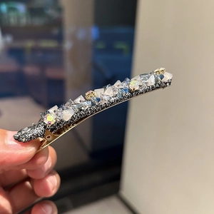 Détail d'une pince à cheveux dorée avec tissu noir et cristaux de strass bleus