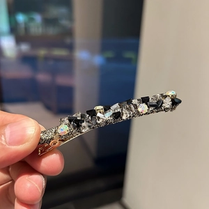 Détail macro d'une barrette à cheveux avec strass noirs et irisés sur base en métal tressé
