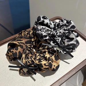 Détail de chouchous léopard avec nœuds en cuir et pendentifs en métal doré