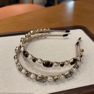 Detailed view of pearl and rhinestone hairbands on a textured fabric display stand