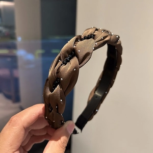 Dettaglio di un cerchietto intrecciato marrone in raso con strass e perline nere