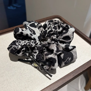 Détail du chouchou à imprimé léopard avec nœud en similicuir et breloque dorée