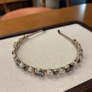 Close-up of elegant headband featuring cream pearls and grey crystals in gold claw settings