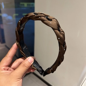Dettaglio di un cerchietto intrecciato marrone con strass brillanti e perline nere