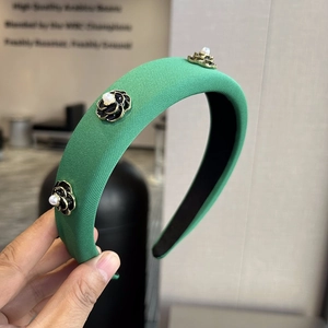Detail of green thick headband with black camellia flowers and white pearl accents