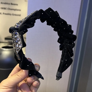 Détail d'un serre-tête en velours avec strass argentés et perles sur tissu plissé