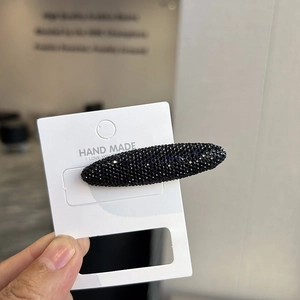 Macro shot of an oval black BB clip encrusted with sparkling rhinestones on a display card