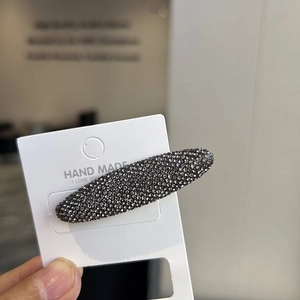 Close-up of handmade oval hair clip with dense dark grey rhinestones on a display card