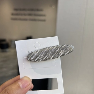 Macro view of an oval-shaped rhinestone hair clip on a white display card with sparkling gems
