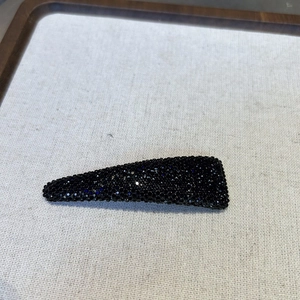 Close-up of teardrop shaped black rhinestone hair clip with star-like glitter detail