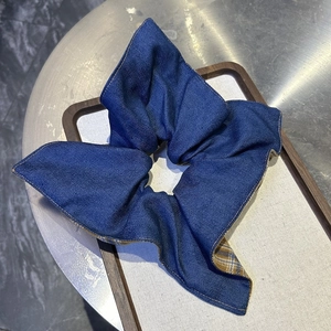 Détail d'un chouchou en jean bleu avec doublure à carreaux jaunes sur support blanc