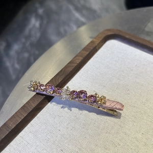 Detail of pink crystal hair clip featuring purple gemstones and woven ribbon wrap